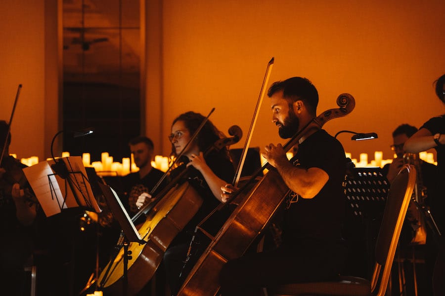 A man and a woman playing the cello sitting down in a candlelit setting.