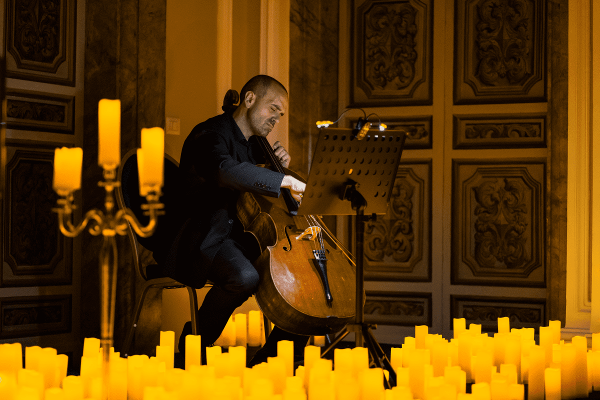 Male musician playing cello while surrounded by candles