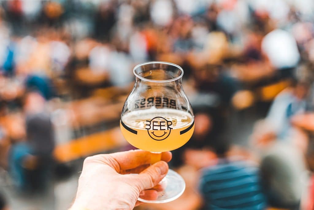 glass of beer held aloft in front of blurred crowds