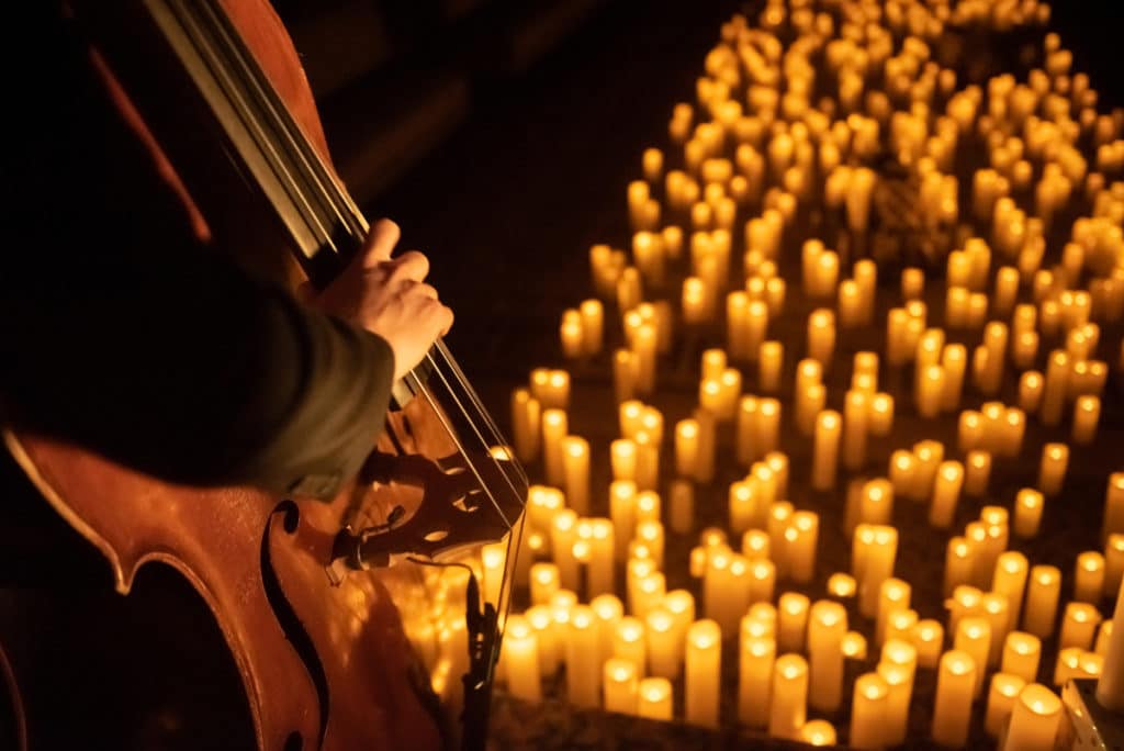A close-up of the base of a cello with candles in the background.