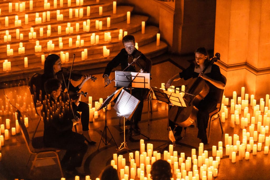 A string quartet playing on stage while surrounded by candlelight.