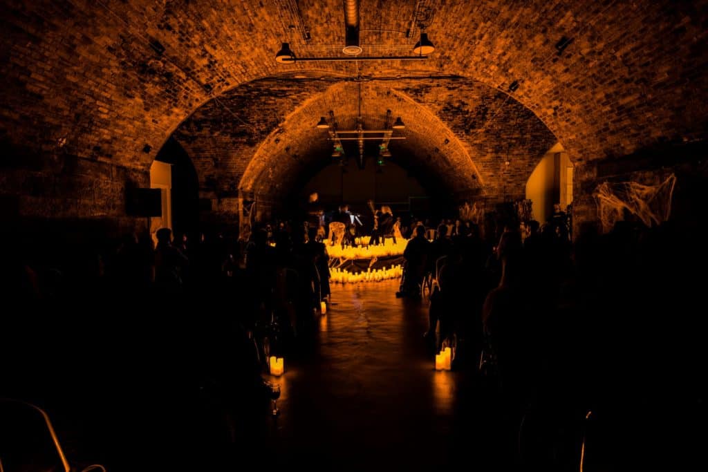A dark image revealing the stony interior of Platform in Glasgow where a string quartet is performing surrounded by candles.