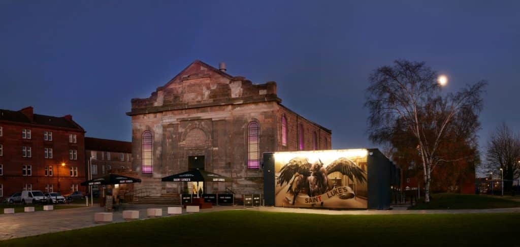 Exterior of St Luke's venue under evening lighting with a large winged mural on display 